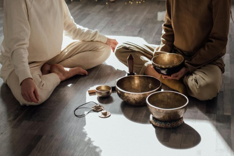 Twee mensen zitten in kleermakerszit bij klankschalen op een houten vloer