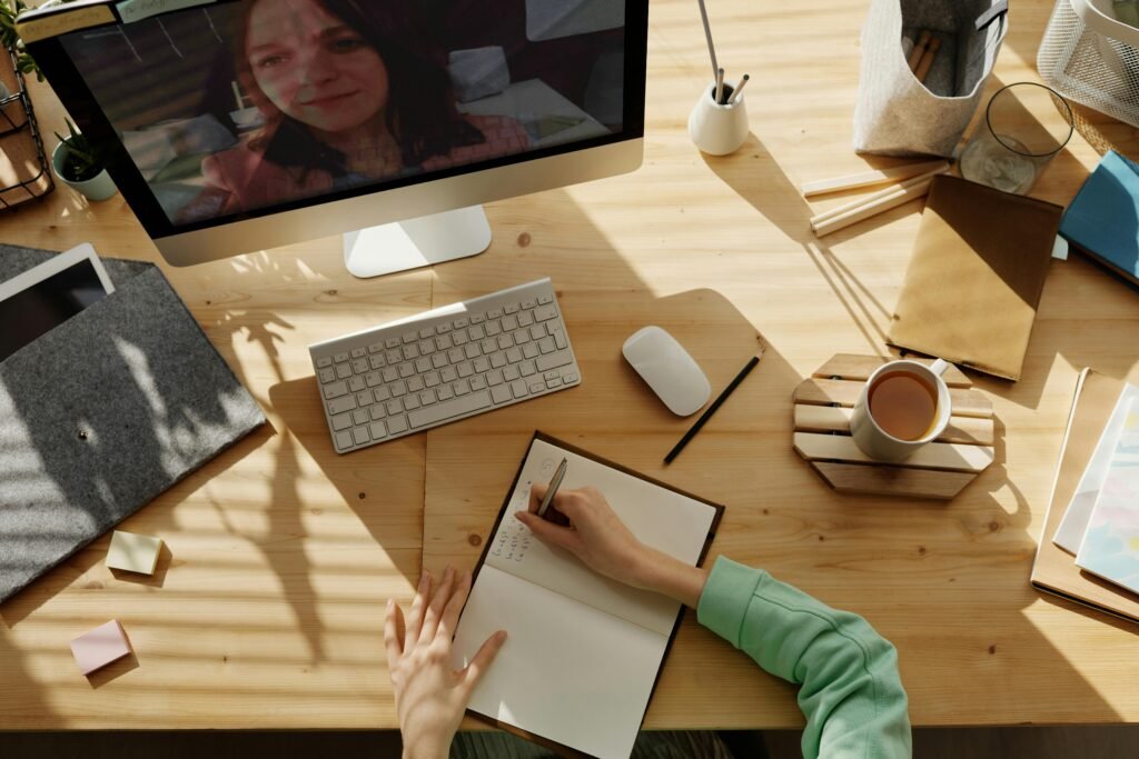 Bureau van bovenaf met notitieboek, koffie en een online sessie op het scherm