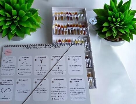 Werkboek met symbolenkaart en flesjes remedie tussen twee vetplanten op een wit bureau