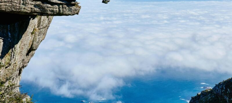 Wandelaar zit op een rotspunt hoog boven de wolken met uitzicht op de kust