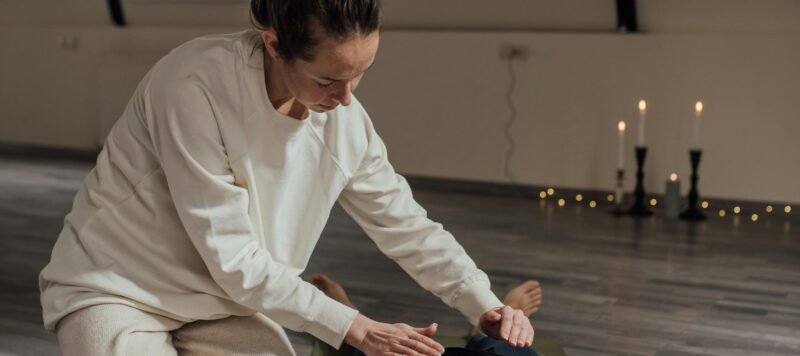 Behandelaar legt haar handen op de buik van een vrouw die op een yogamat ligt, met kaarsen ernaast