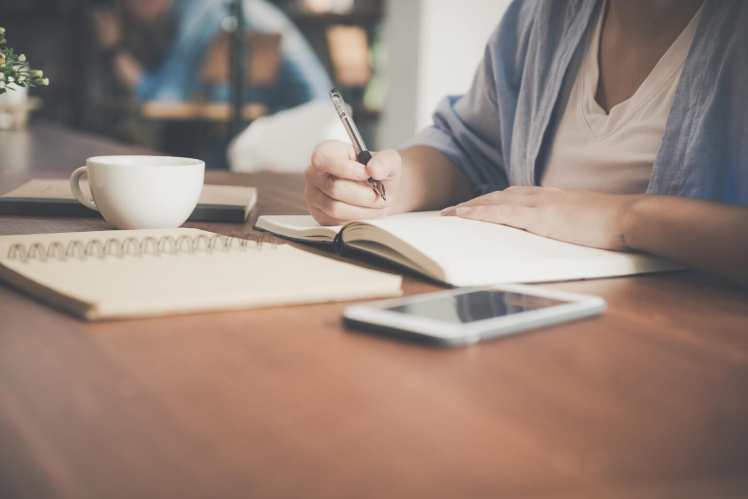 Persoon schrijft in een notitieboek aan tafel met een kop koffie