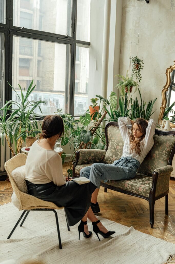 Twee vrouwen in gesprek bij een groot raam met planten