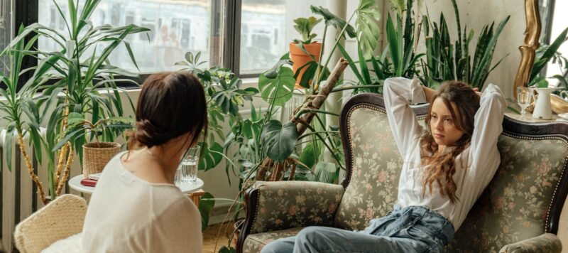 Twee vrouwen in gesprek bij een groot raam met planten