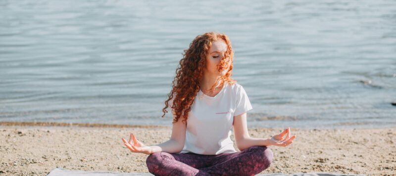 Vrouw mediteert op een yogamat aan het water