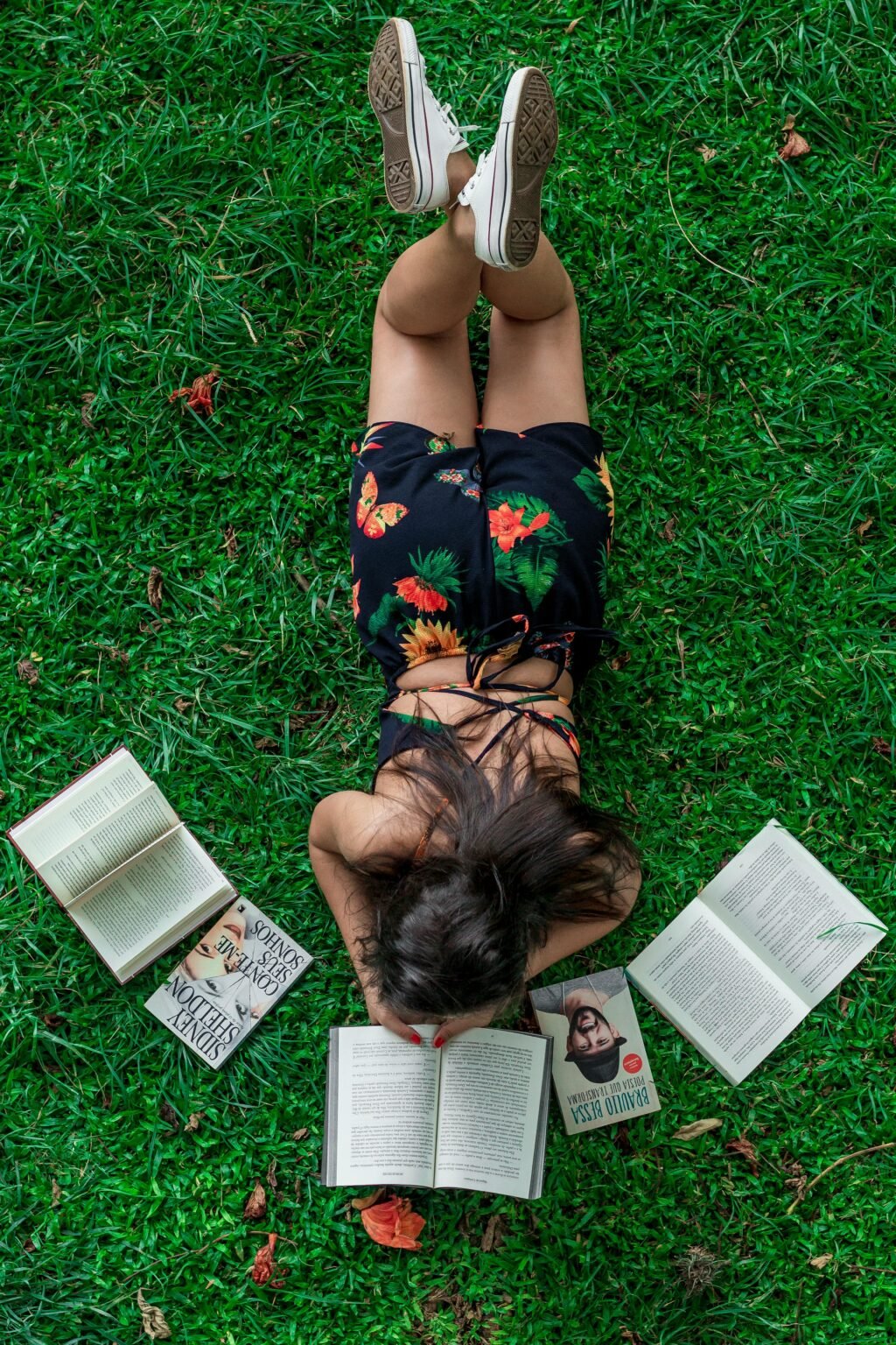 Persoon ligt in het gras te lezen tussen opengeslagen boeken
