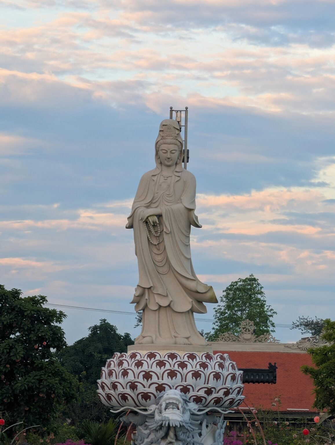 Houten Kwan Yin-beeld met roze lotusbloem in warm ochtendlicht.