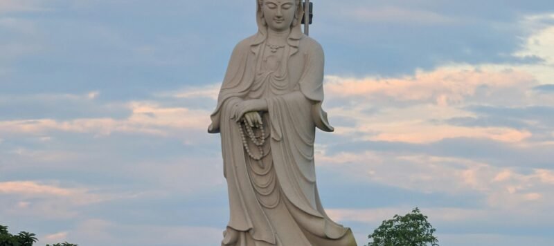 Houten Kwan Yin-beeld met roze lotusbloem in warm ochtendlicht.