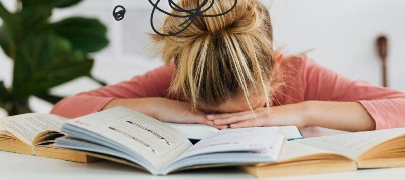 Vermoeide vrouw rust met haar hoofd op een stapel boeken