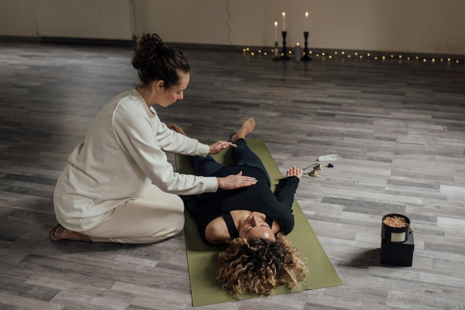 Behandelaar geeft reiki aan een vrouw op een yogamat bij kaarslicht