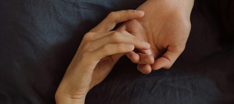 Twee verstrengelde handen op donker beddengoed