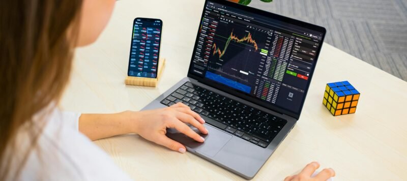Vrouw volgt beursgrafieken op een laptop en telefoon