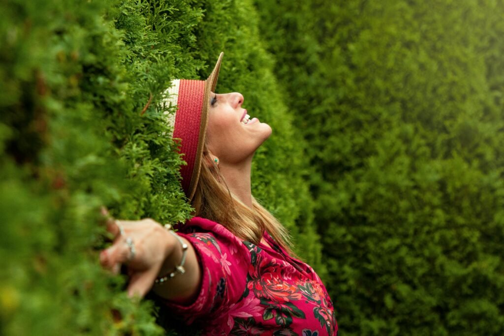 Vrouw met hoed heft haar gezicht naar het licht tussen hoge groene heggen