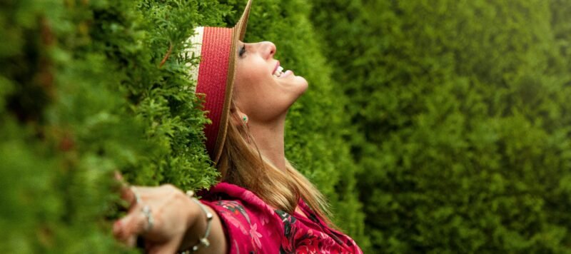 Vrouw met hoed heft haar gezicht naar het licht tussen hoge groene heggen