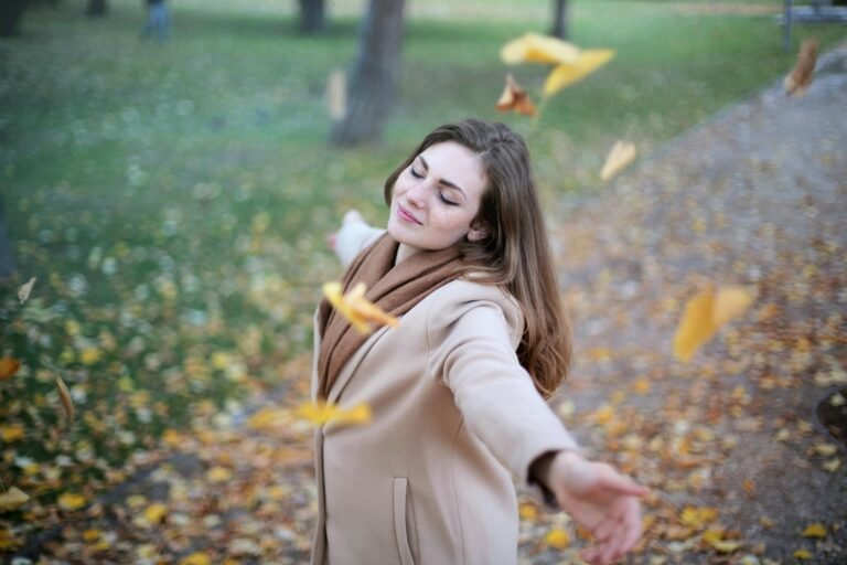 Vrouw met gespreide armen tussen dwarrelende herfstbladeren in het park