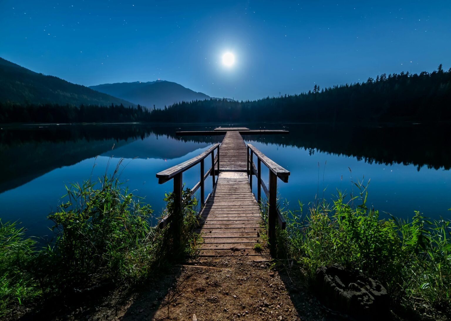 Houten steiger over een spiegelglad meer bij volle maan