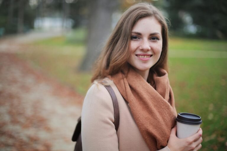 Glimlachende vrouw met een koffiebeker in een herfstpark