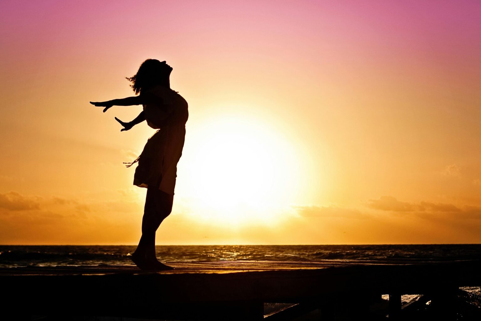 Silhouet van een dansende vrouw bij zonsondergang aan zee