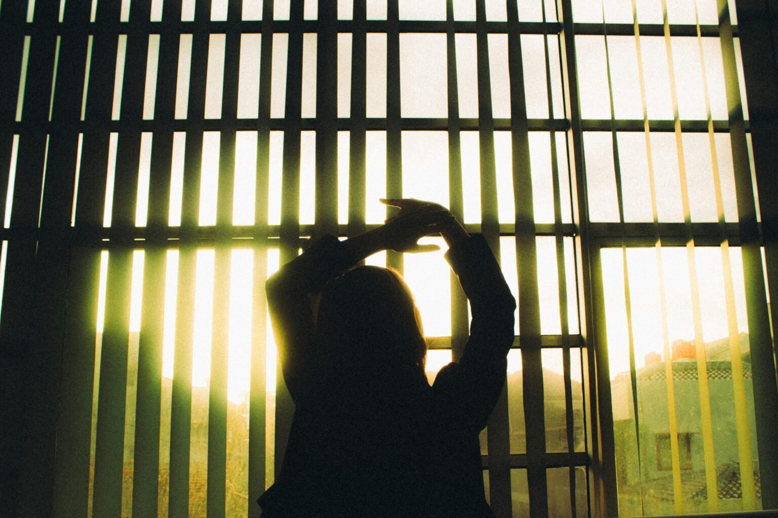 Silhouet van een vrouw in warm tegenlicht achter houten lamellen