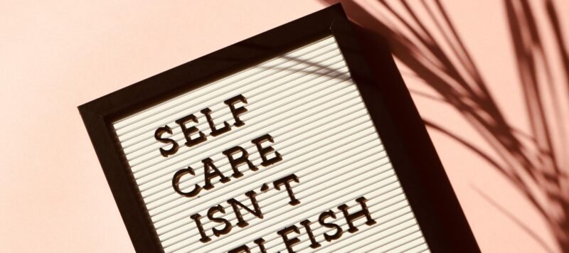 Letterbord met de tekst 'self care isn't selfish' tegen een roze muur