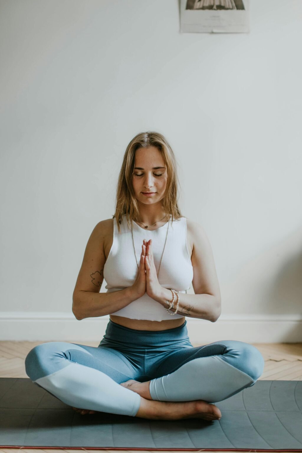 Vrouw mediteert in kleermakerszit op een yogamat met haar handen voor haar hart