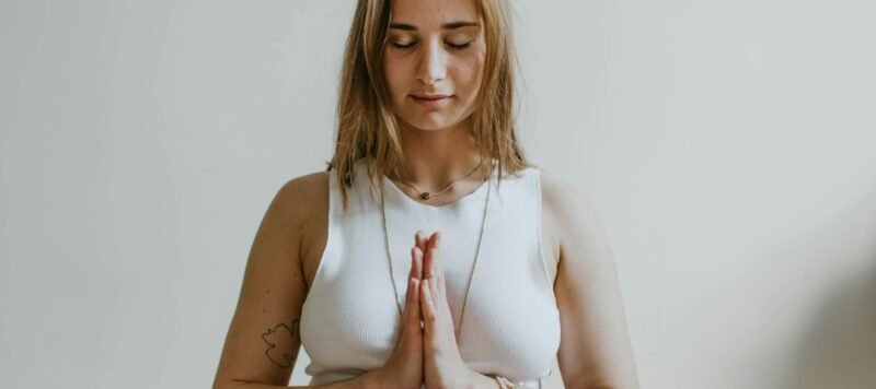 Vrouw mediteert in kleermakerszit op een yogamat met haar handen voor haar hart
