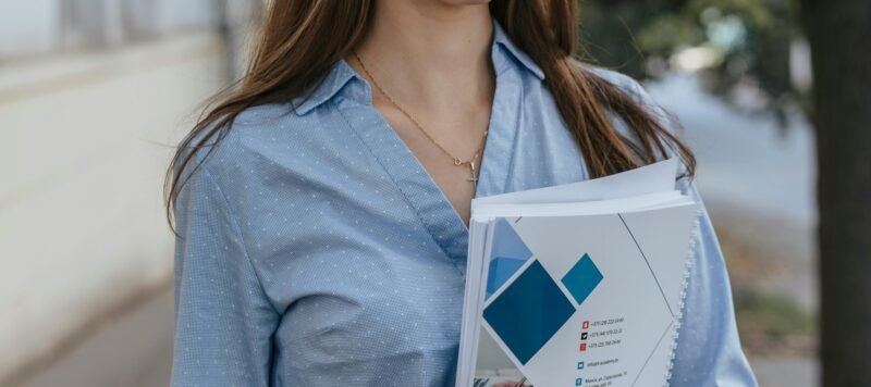 Vrouw in blouse houdt een map met documenten vast op straat