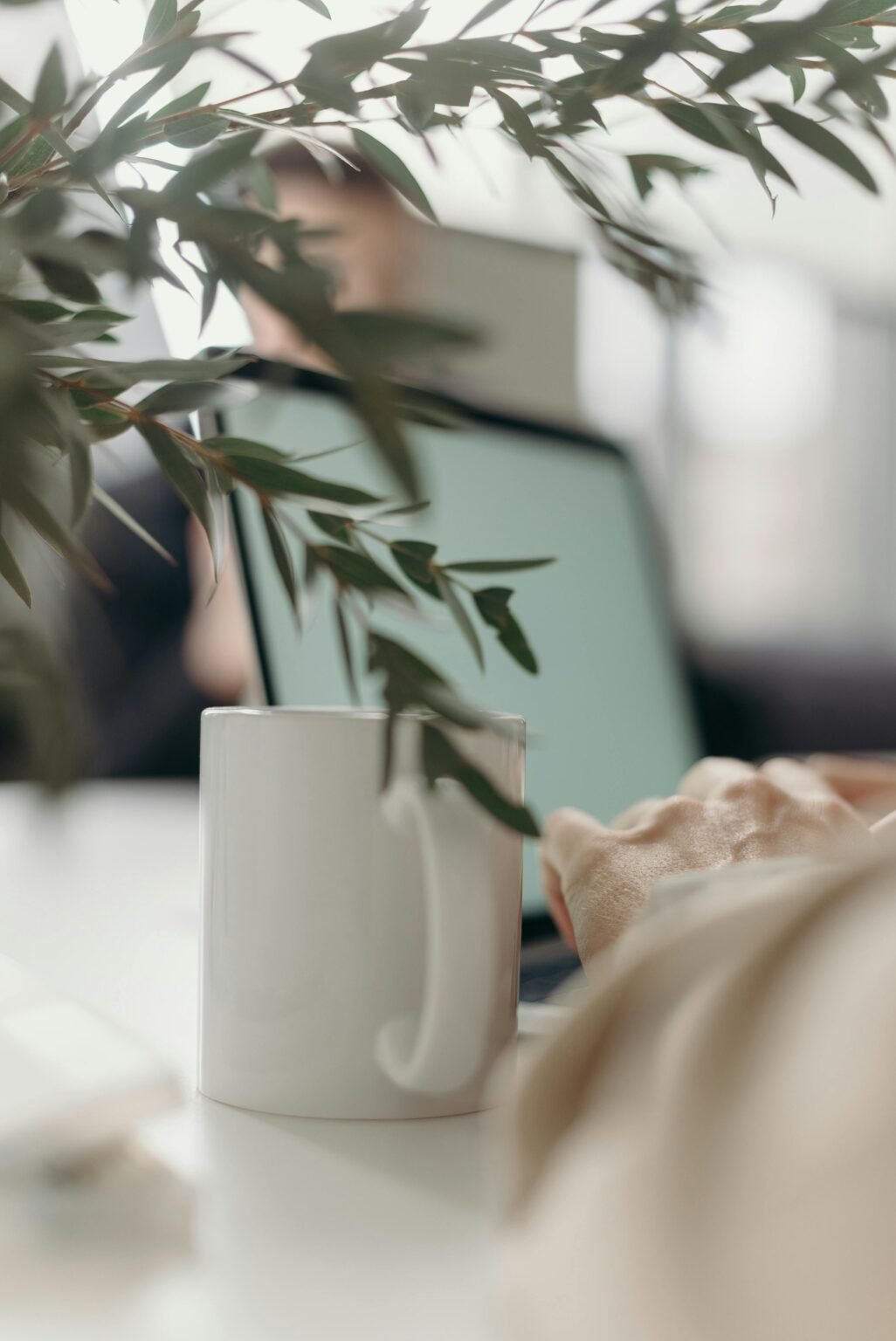 Kop koffie en een tak groen op een bureau, met een laptop op de achtergrond