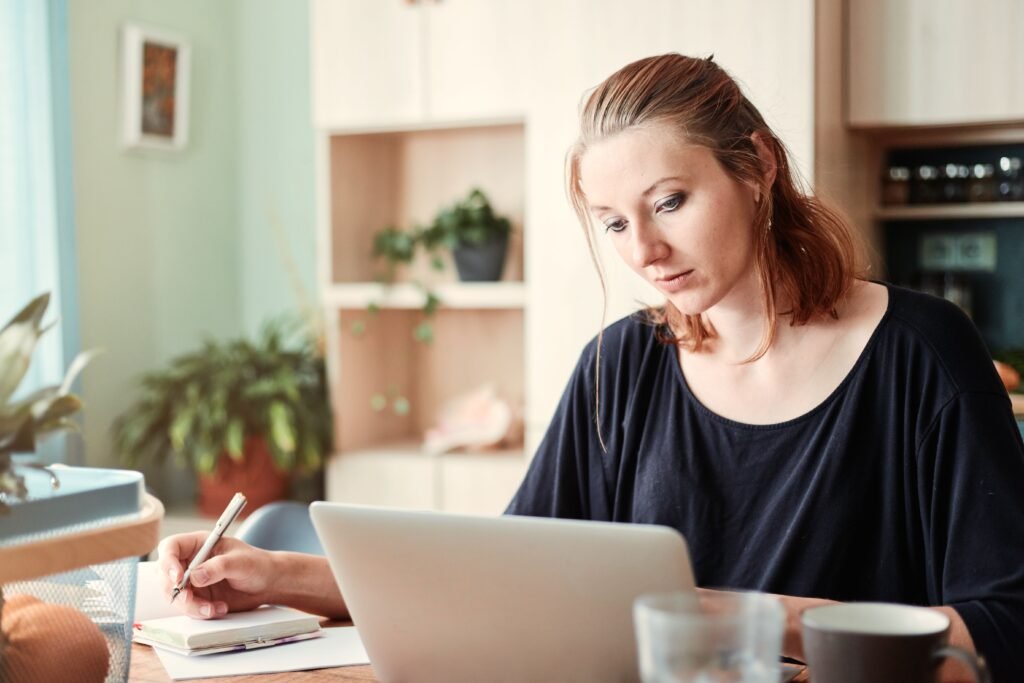 Vrouw achter haar laptop maakt aantekeningen terwijl ze opleidingen vergelijkt aan de keukentafel