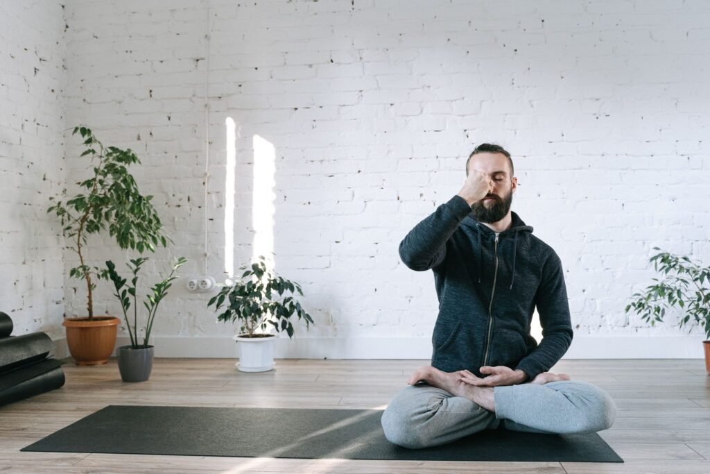 Man zit in kleermakerszit op een yogamat en sluit een neusgat af tijdens een ademoefening in een lichte studio