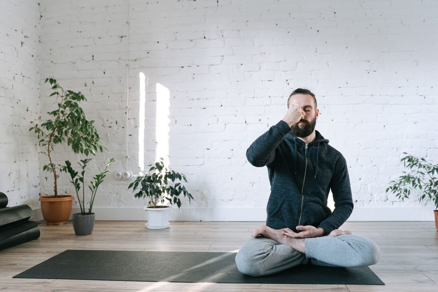 Man zit in kleermakerszit op een yogamat en sluit een neusgat af tijdens een ademoefening in een lichte studio