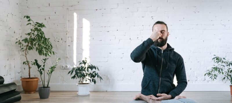 Man zit in kleermakerszit op een yogamat en sluit een neusgat af tijdens een ademoefening in een lichte studio