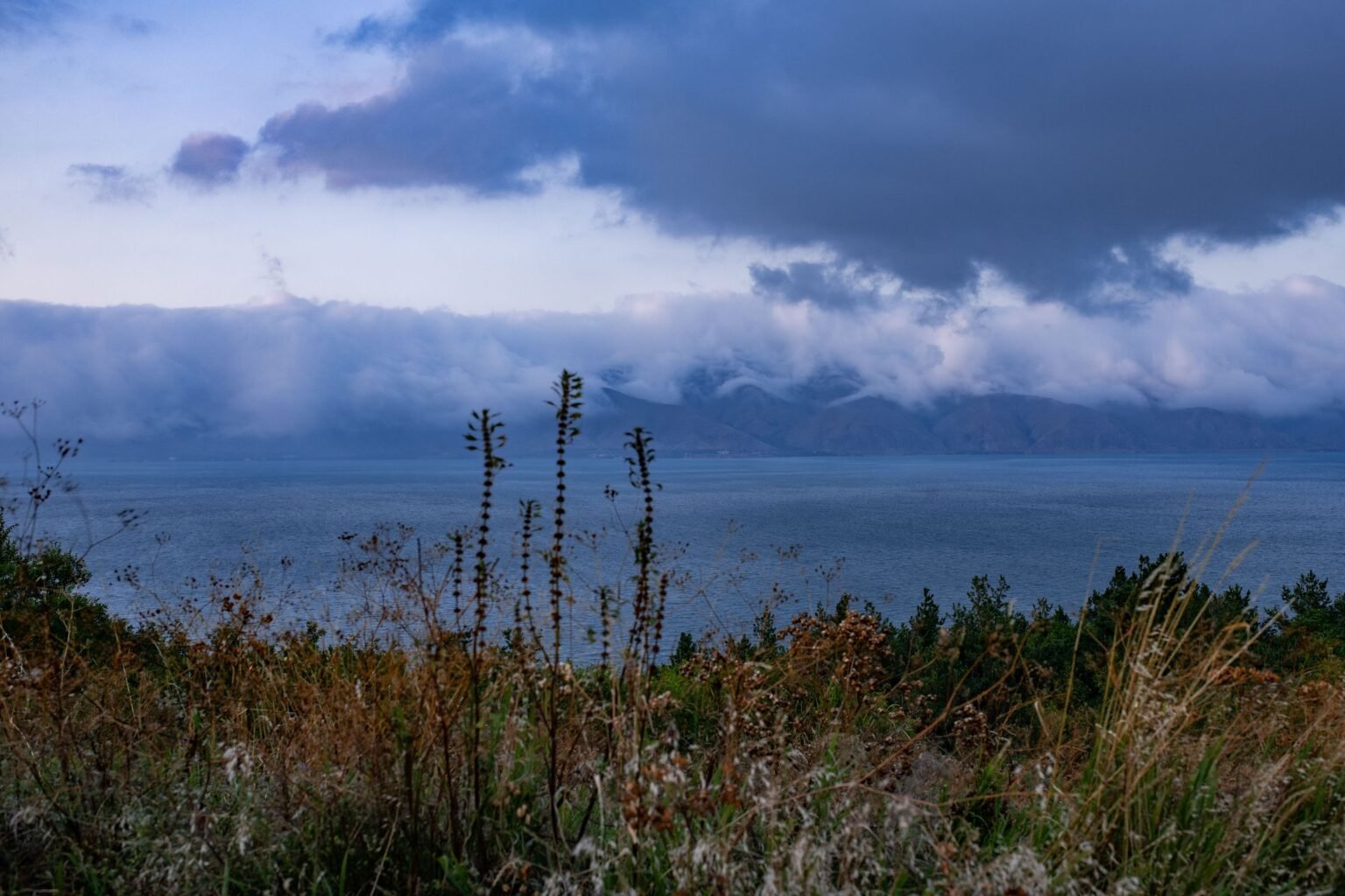 Bergen en wolken boven een meer, met gras op de voorgrond
