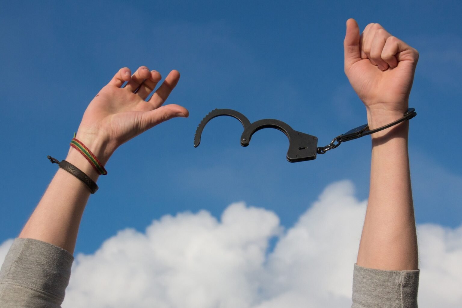 Twee handen breken een handboei doormidden tegen een blauwe lucht