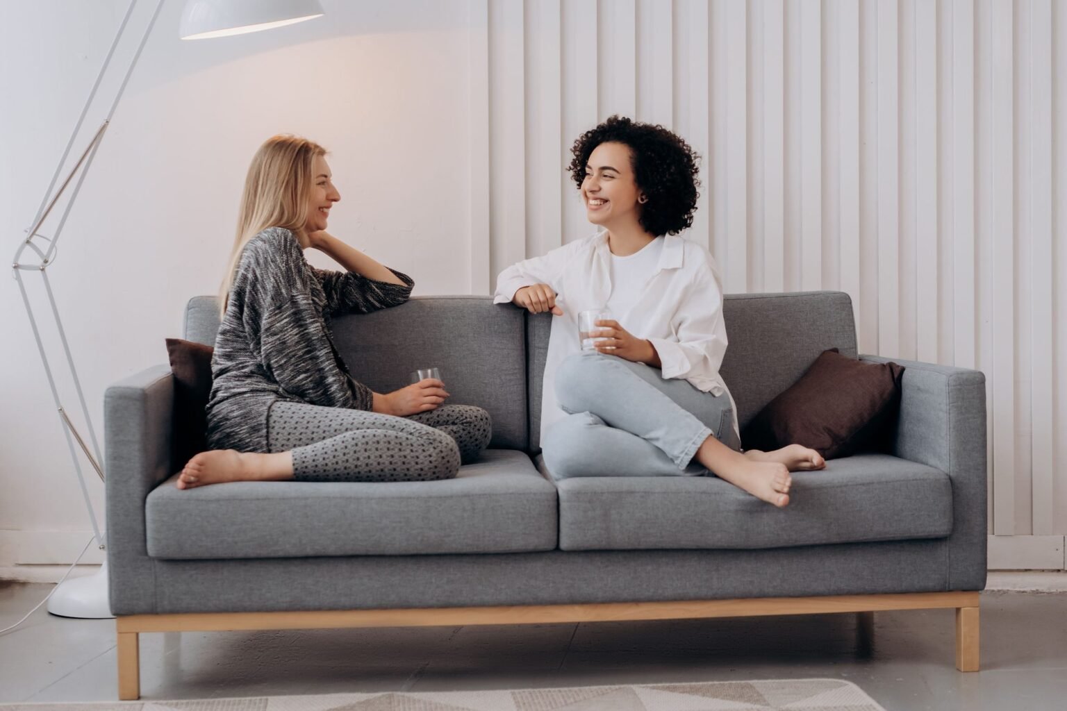 Twee vrouwen zitten ontspannen in gesprek op een bank in een lichte woonkamer
