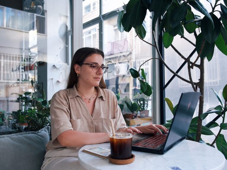 Vrouw volgt een online videoles op haar laptop aan een tafel bij het raam