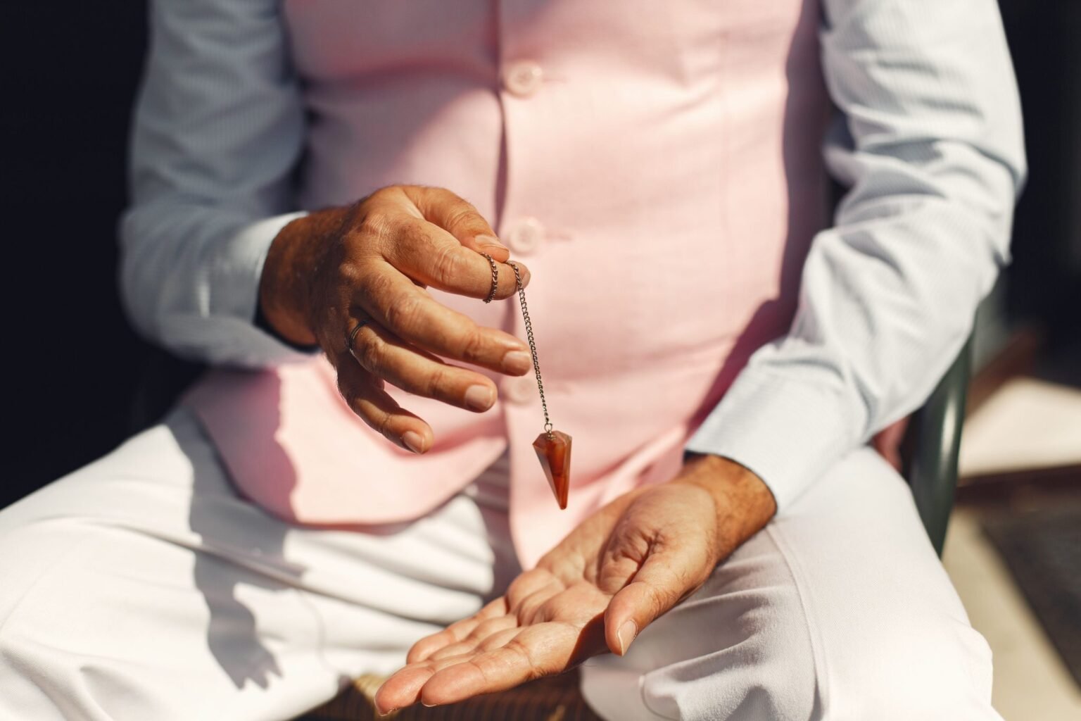 Hand houdt een pendel aan een ketting boven een geopende handpalm