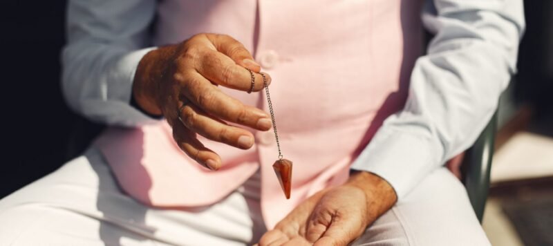 Hand houdt een pendel aan een ketting boven een geopende handpalm