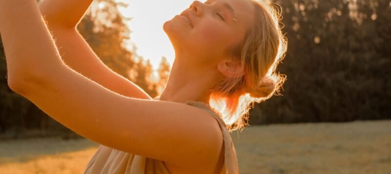 Vrouw met haar armen omhoog en haar gezicht naar de zon in een veld bij zonsondergang