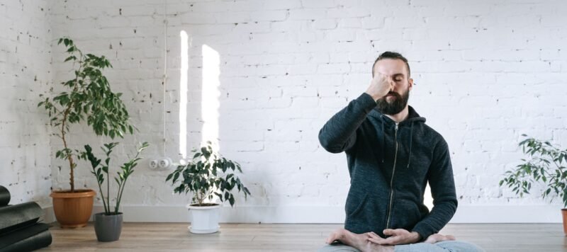 Man in kleermakerszit doet een ademhalingsoefening in een lichte yogastudio