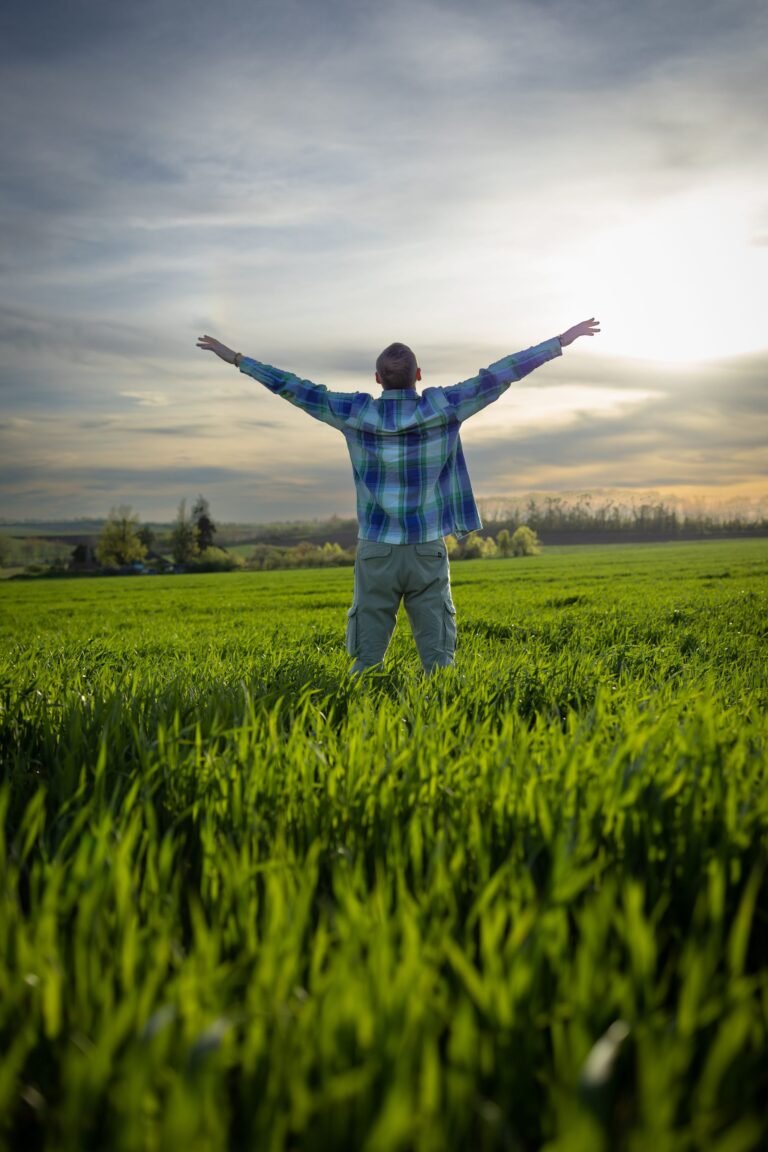Man staat met wijd gespreide armen in een groen veld bij zonsondergang