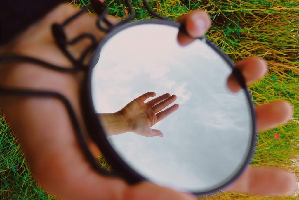 Ronde spiegel in het gras waarin een uitgestrekte hand en de lucht weerspiegelen