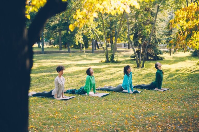 Vijf mensen zitten op matten in het gras onder herfstbomen