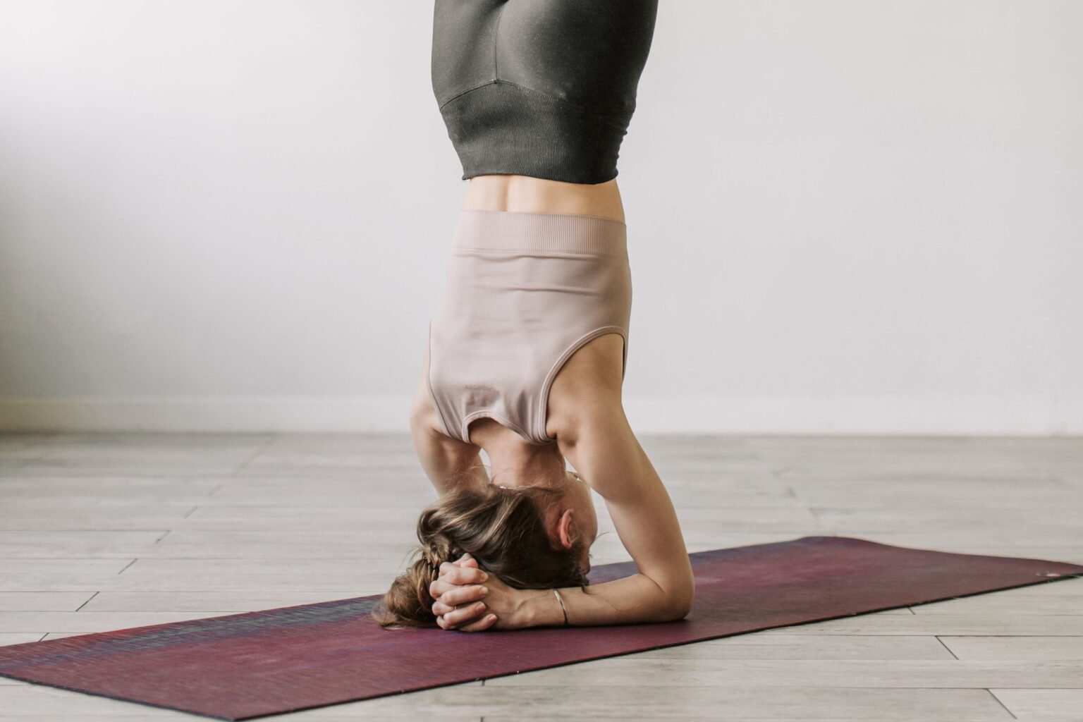 Vrouw staat ondersteboven op haar schouders op een yogamat