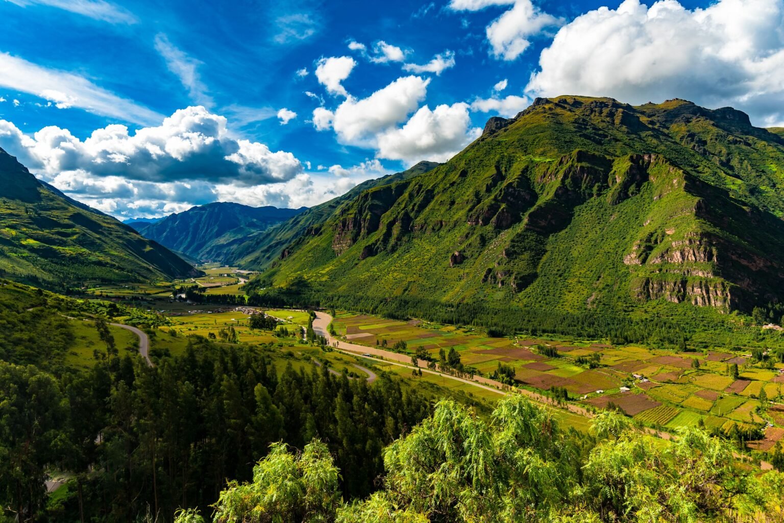 Groene bergvallei in de Andes met akkers en een rivier onder een blauwe lucht