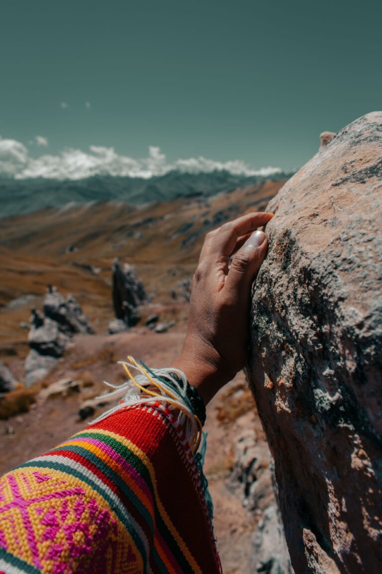 Hand in een geweven Andes-poncho rust op een rots, met bergen op de achtergrond