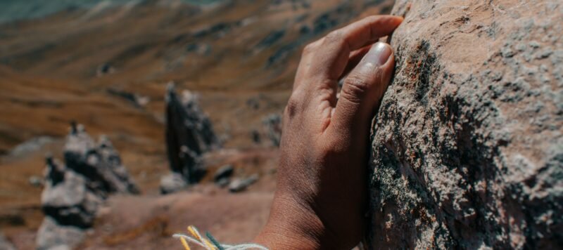 Hand in een geweven Andes-poncho rust op een rots, met bergen op de achtergrond